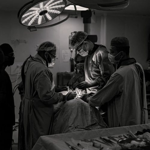 Team of surgeons in an operating room conducting surgery in black and white.